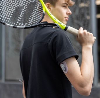 Een tiener met diabetes type 1 speelt tennis, met zijn CGM Dexcom G6-sensor